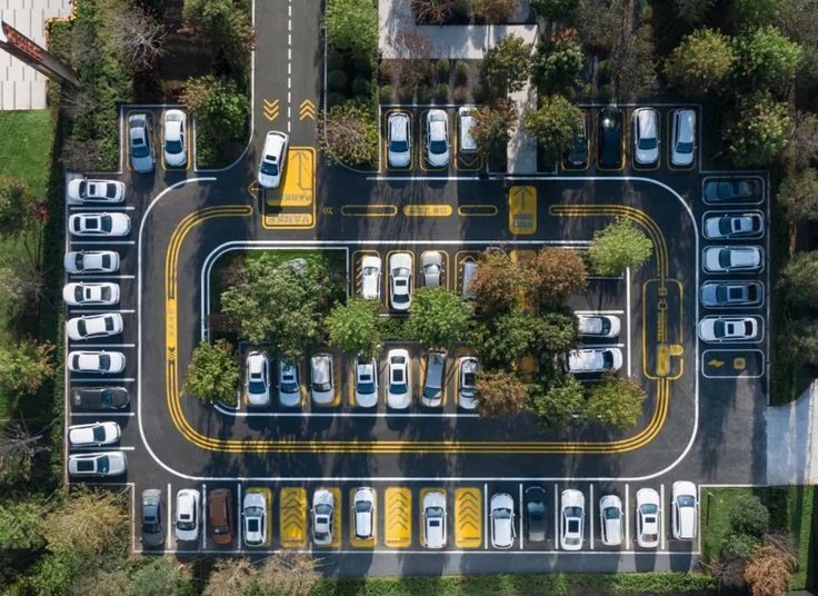 an aerial view of a parking lot with cars parked on it and trees in the background