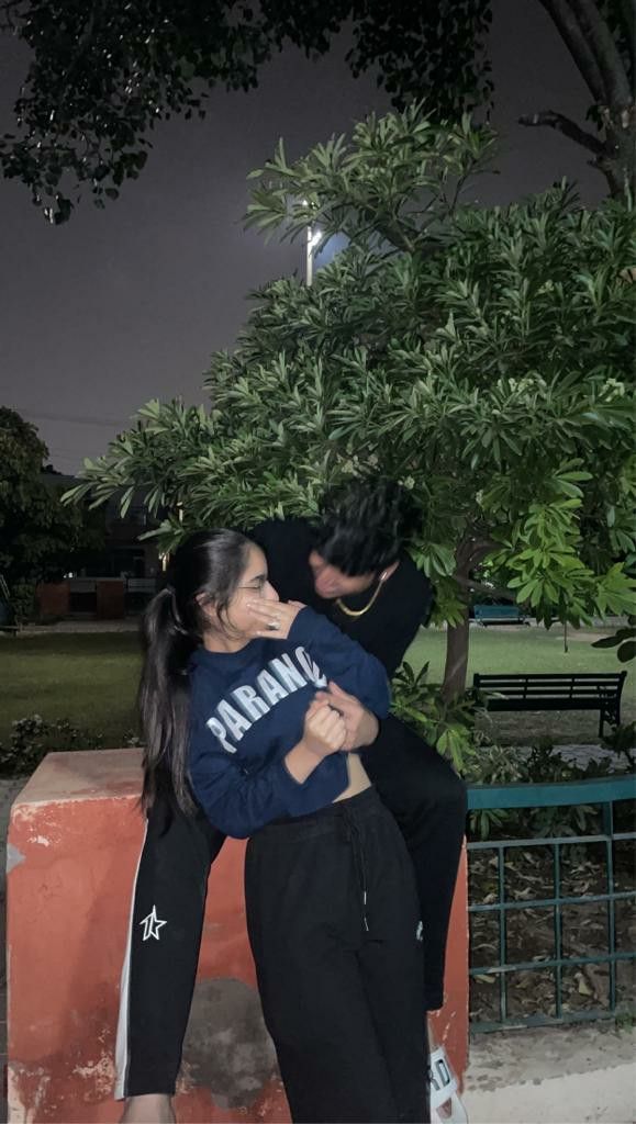 two people hugging each other in front of trees and bench at night with one person leaning on the woman's shoulder