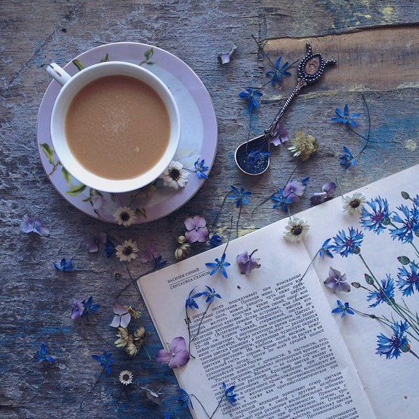 a cup of coffee next to an open book and spoons on a table with flowers