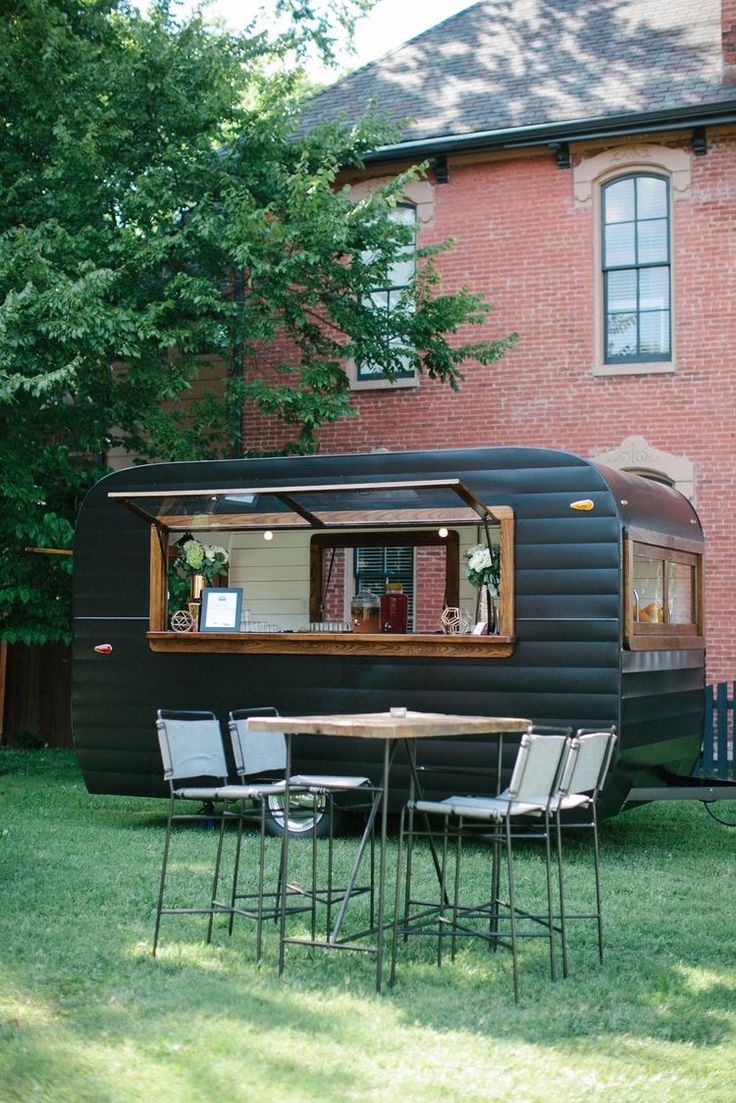 an old trailer converted into a house with chairs and table in the grass next to it