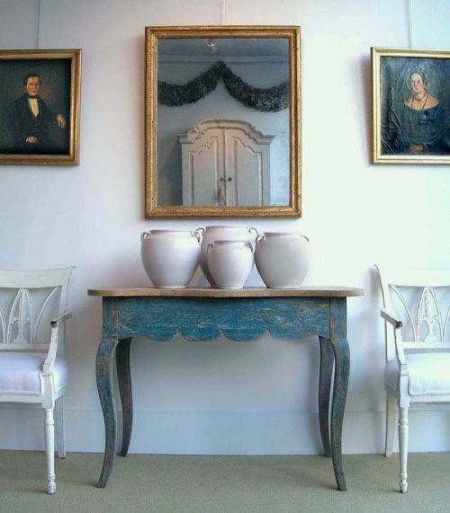 three white vases sitting on top of a blue table in front of two paintings