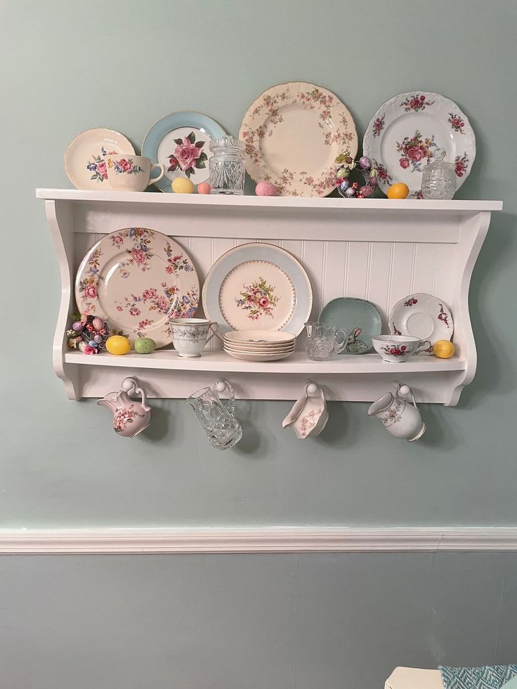 a white shelf filled with plates and dishes on top of it's sides next to a blue wall