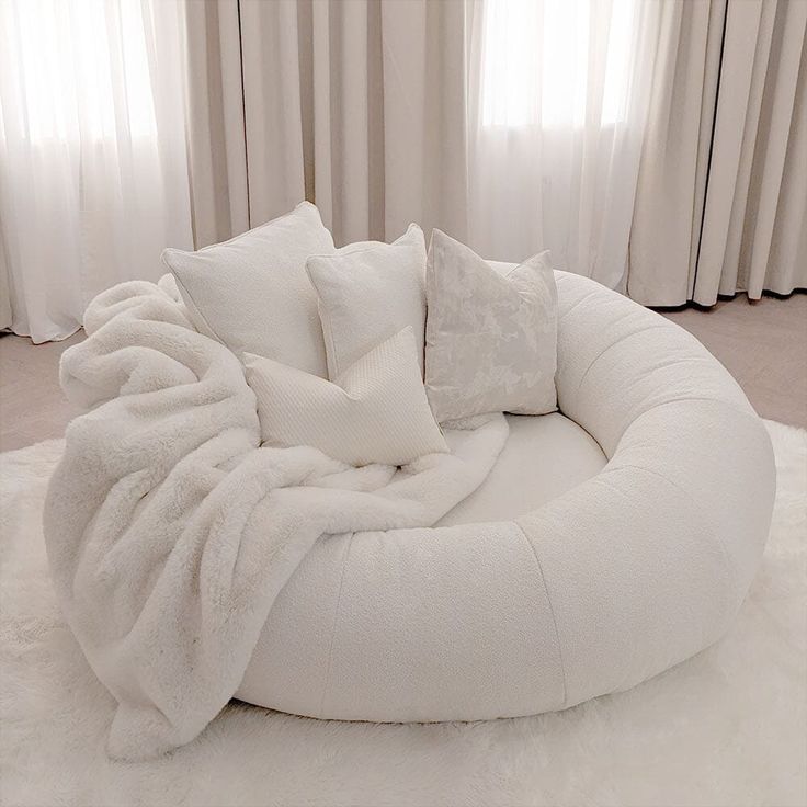 a white round bed with pillows on top of it in front of curtains and drapes