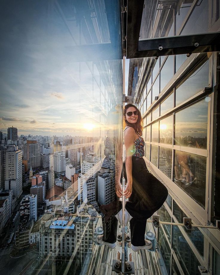 a woman standing on the edge of a high rise building in front of cityscape