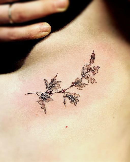 a woman's lower back tattoo with holly leaves and berries on the side ribcage