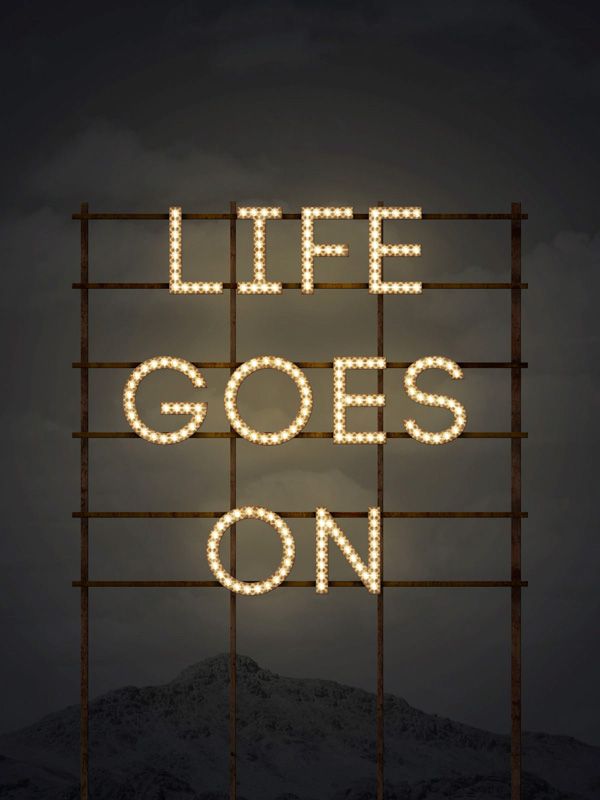 the words life goes on are lit up in front of a dark background with mountains