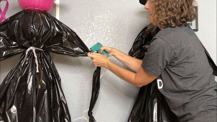 a man in grey shirt and black hat working on a plastic bag mannequin