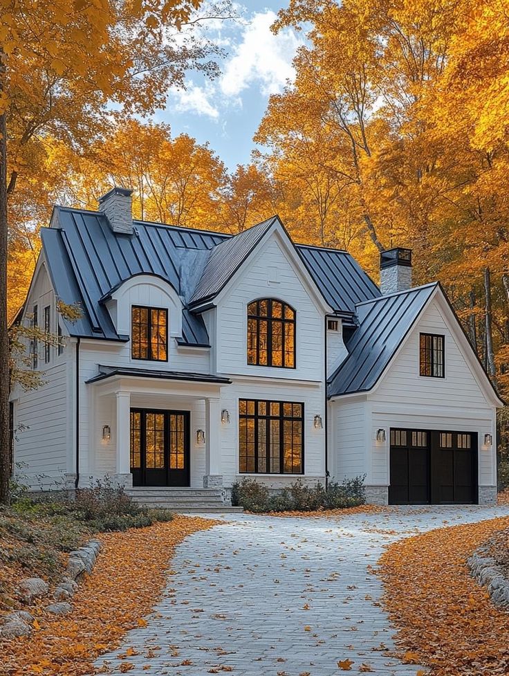 a large white house surrounded by trees with fall leaves on the ground and in front