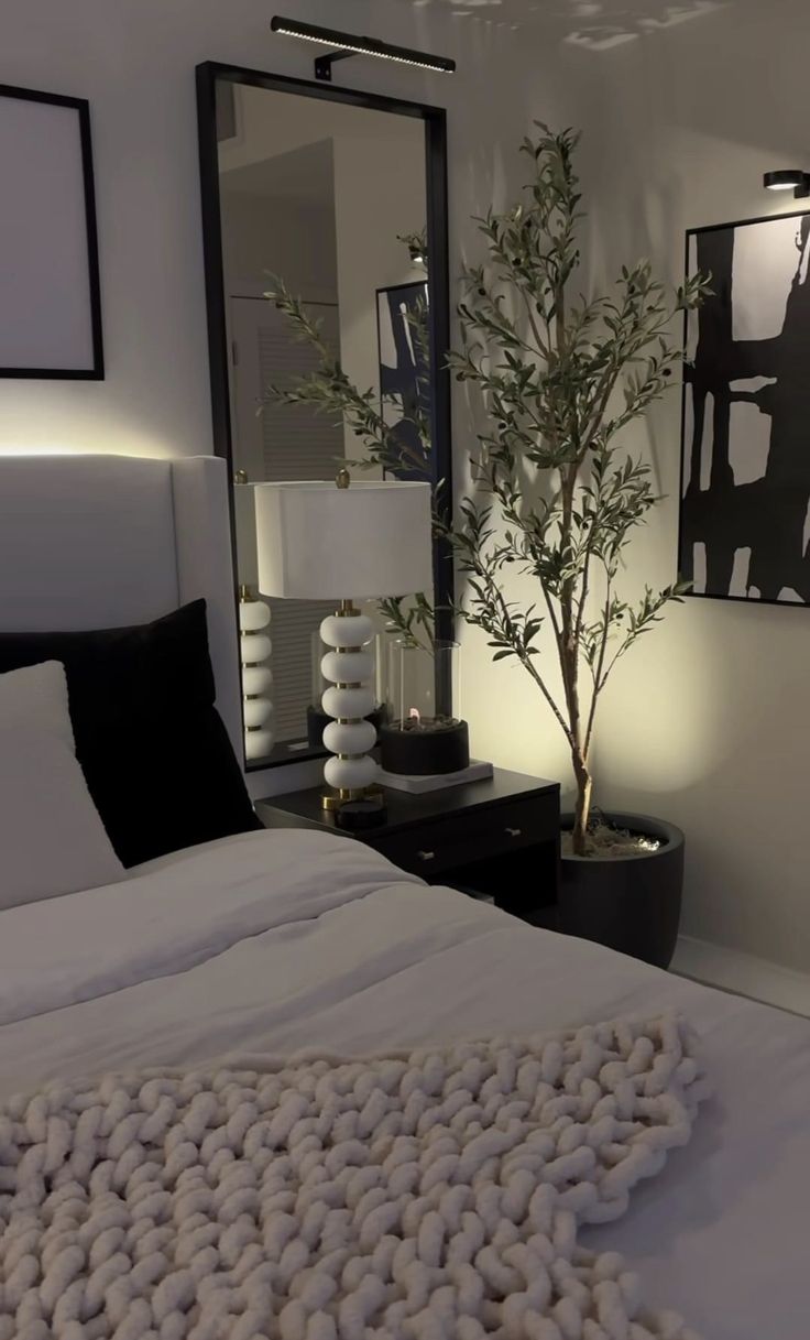 a white bed sitting under a large mirror next to a plant in a vase on top of a table