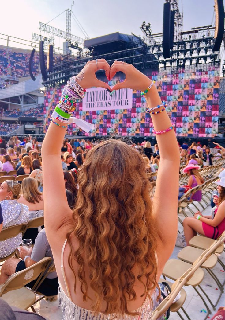 a woman with her hands in the air holding up a sign at a concert or show