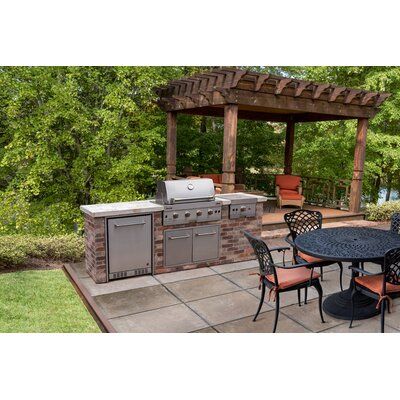 an outdoor kitchen with grill, table and chairs