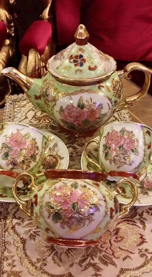 an ornately decorated tea set with pink flowers and gold trimmings sits on a table