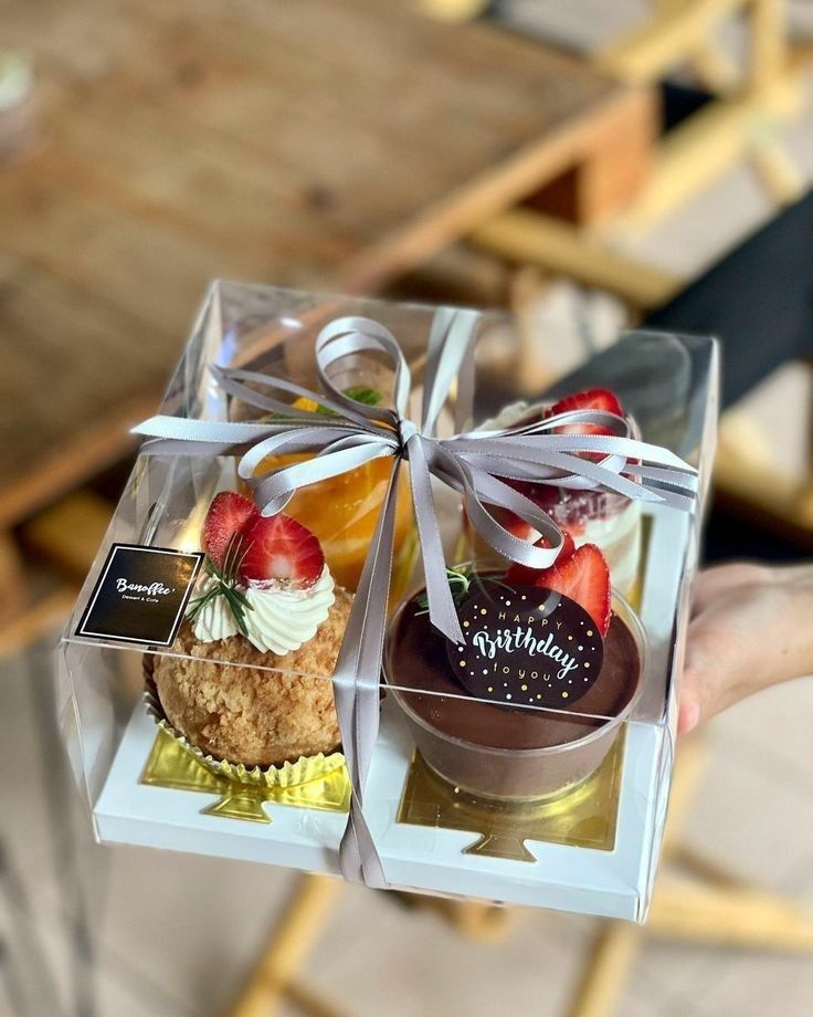 a person is holding two small boxes with desserts in them and one has a bow on it