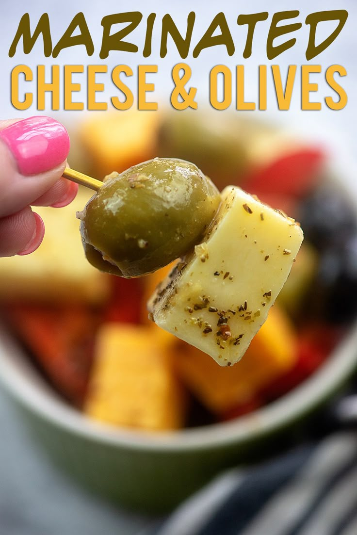 a hand holding a piece of cheese and olives over a bowl of mixed vegetables