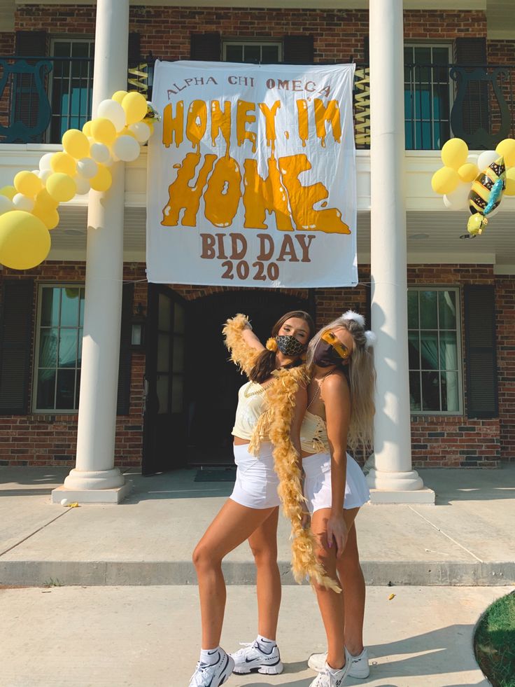 two young women standing in front of a building holding up a sign that says honey i'm home