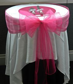 a pink chair sash on top of a white round table with black cloth and silverware