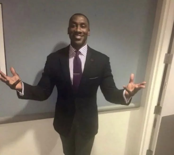 a man wearing a suit and tie standing in front of a wall with his hands out