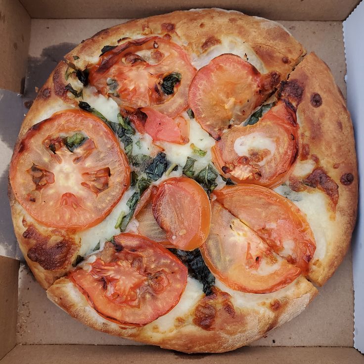 a pizza with tomatoes, spinach and cheese in a box