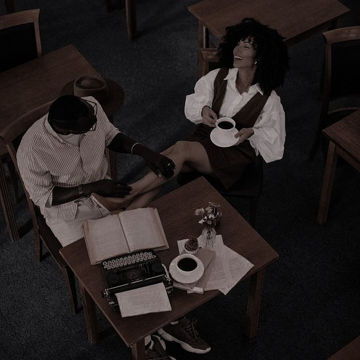 two people sitting at a table with coffee and books