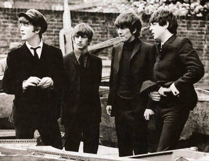 black and white photograph of four young men standing next to each other in front of a car