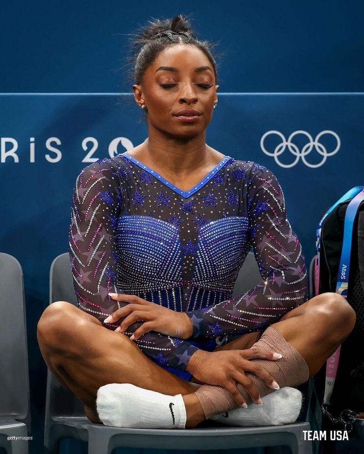 a woman sitting on top of a chair in front of a blue wall with an olympic sign behind her