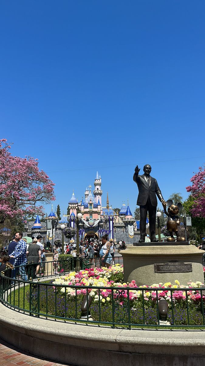 a statue of walt and mickey mouse in front of the disneyland world theme park entrance