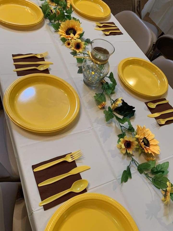 the table is set with yellow plates and sunflowers