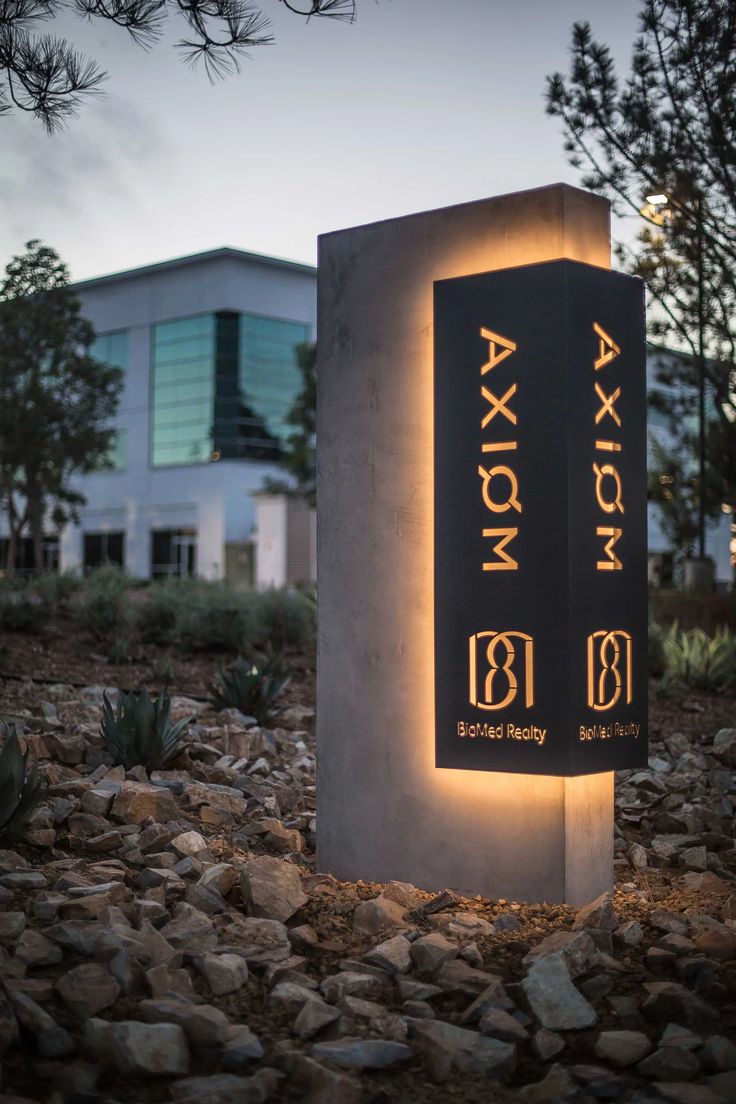 a sign that is sitting in the middle of some rocks and gravel with a building in the background