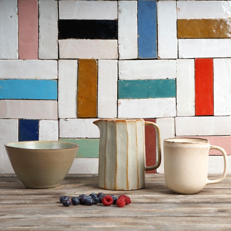 two mugs and one bowl are sitting on a table with colorful tiles behind them