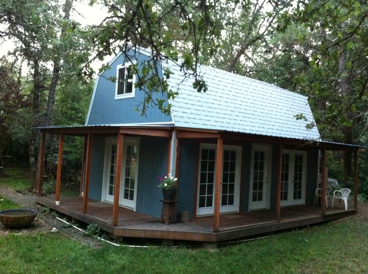 a small blue house sitting on top of a lush green field with lots of trees