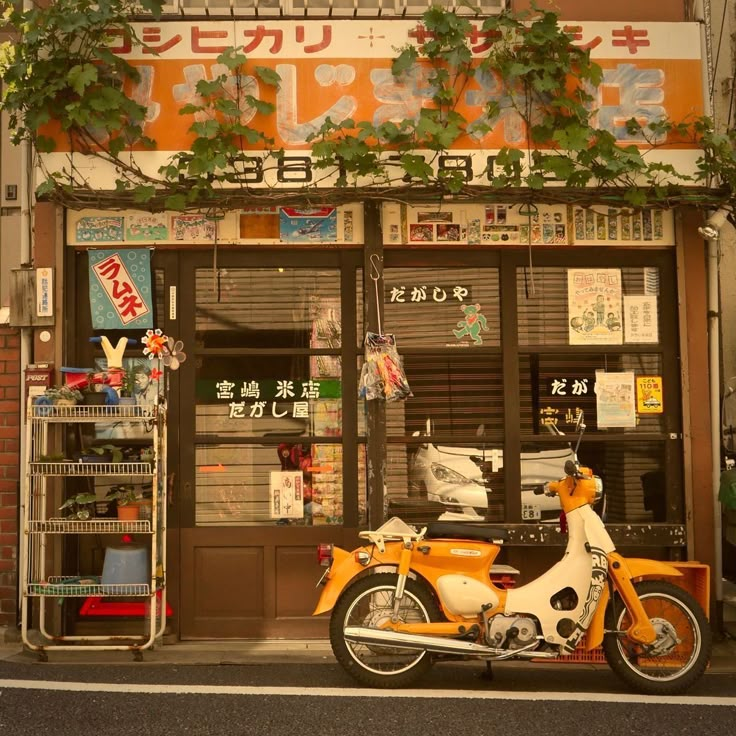 an orange and white motorcycle parked in front of a store with plants growing on the windows