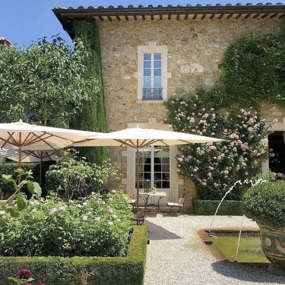 an outdoor area with tables, chairs and umbrellas in front of a stone building