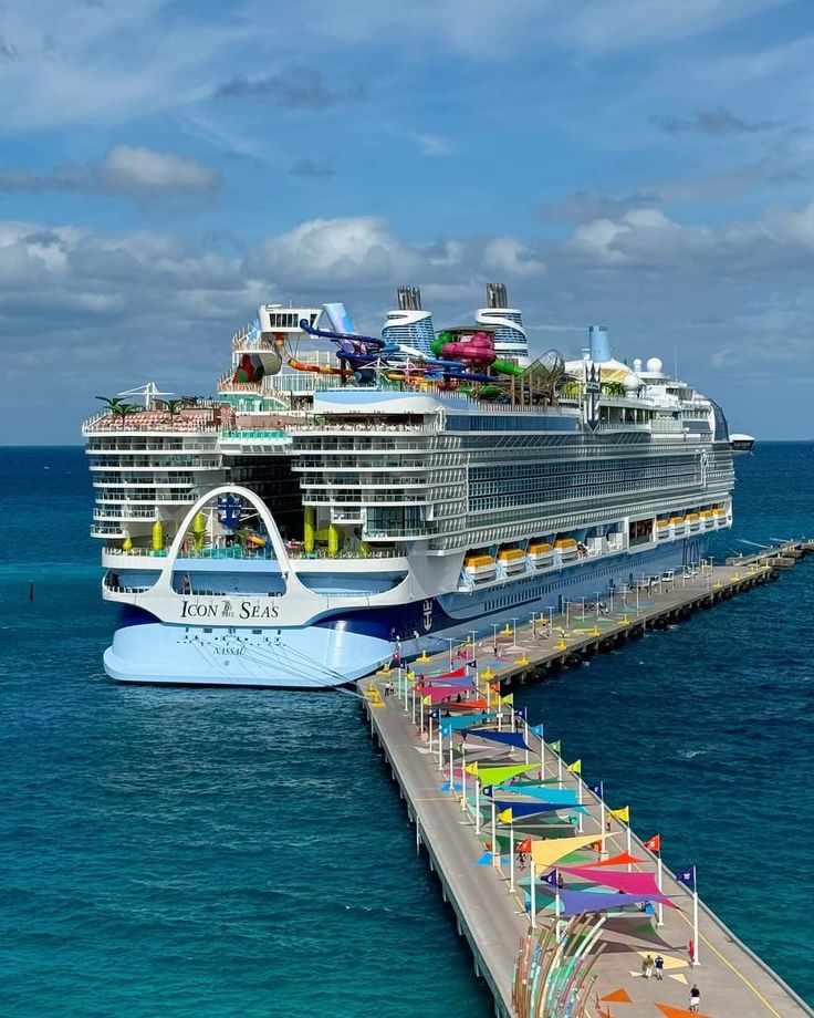 a large cruise ship docked in the ocean next to a pier with colorful umbrellas