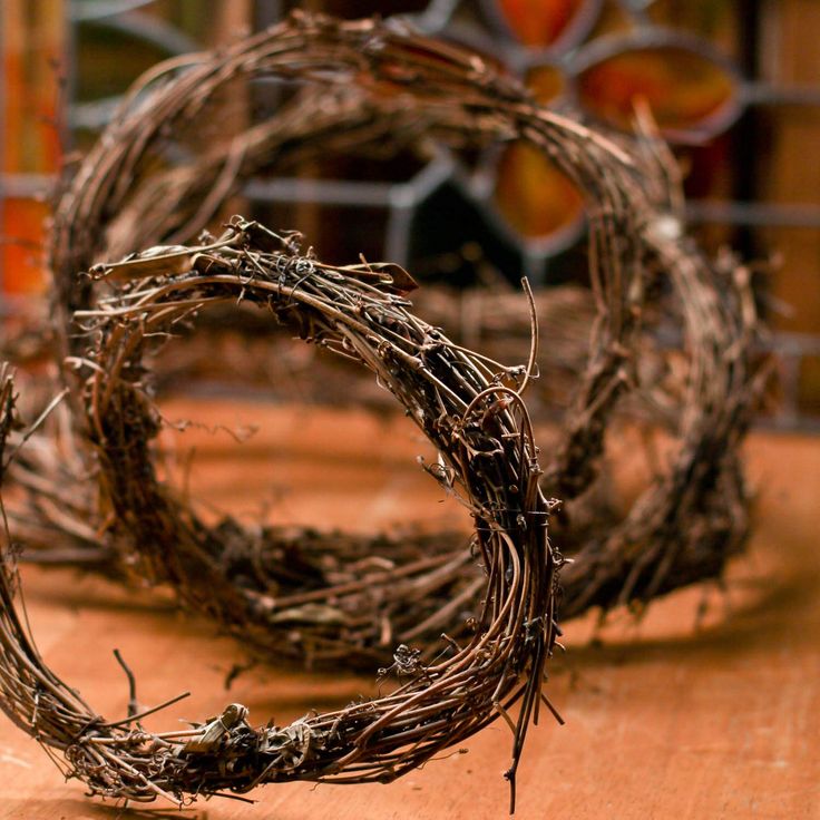 two wreaths made out of twigs sitting on top of a wooden table next to a stained glass window