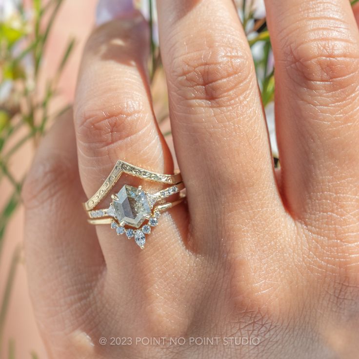 a woman's hand with a ring on it and flowers in the back ground