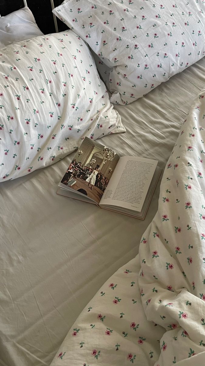 an open book laying on top of a bed with white sheets and pillows next to it