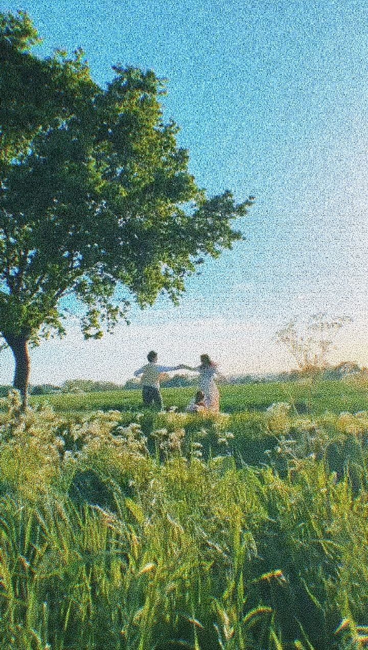 two people standing in the grass under a tree with their arms up to each other