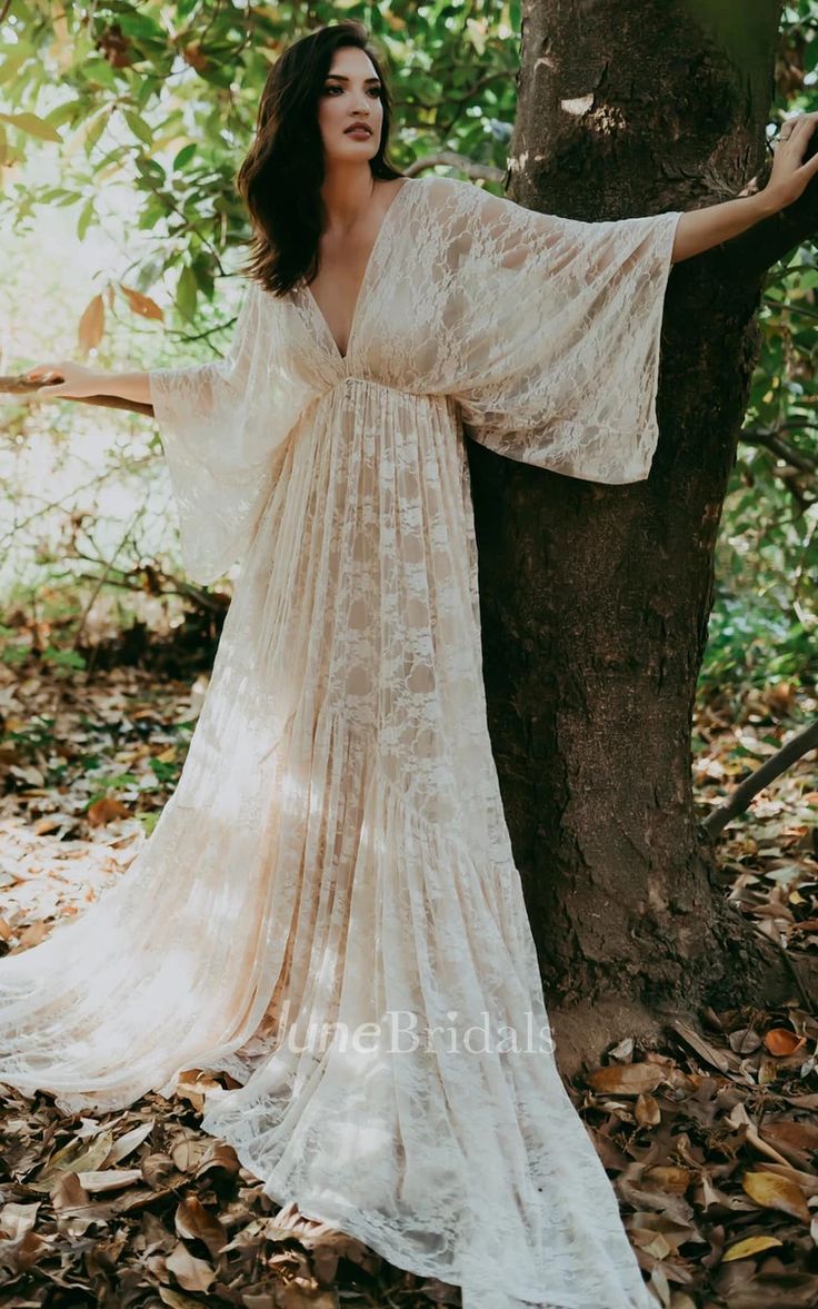 a woman standing next to a tree in a forest wearing a white dress and holding her arms out