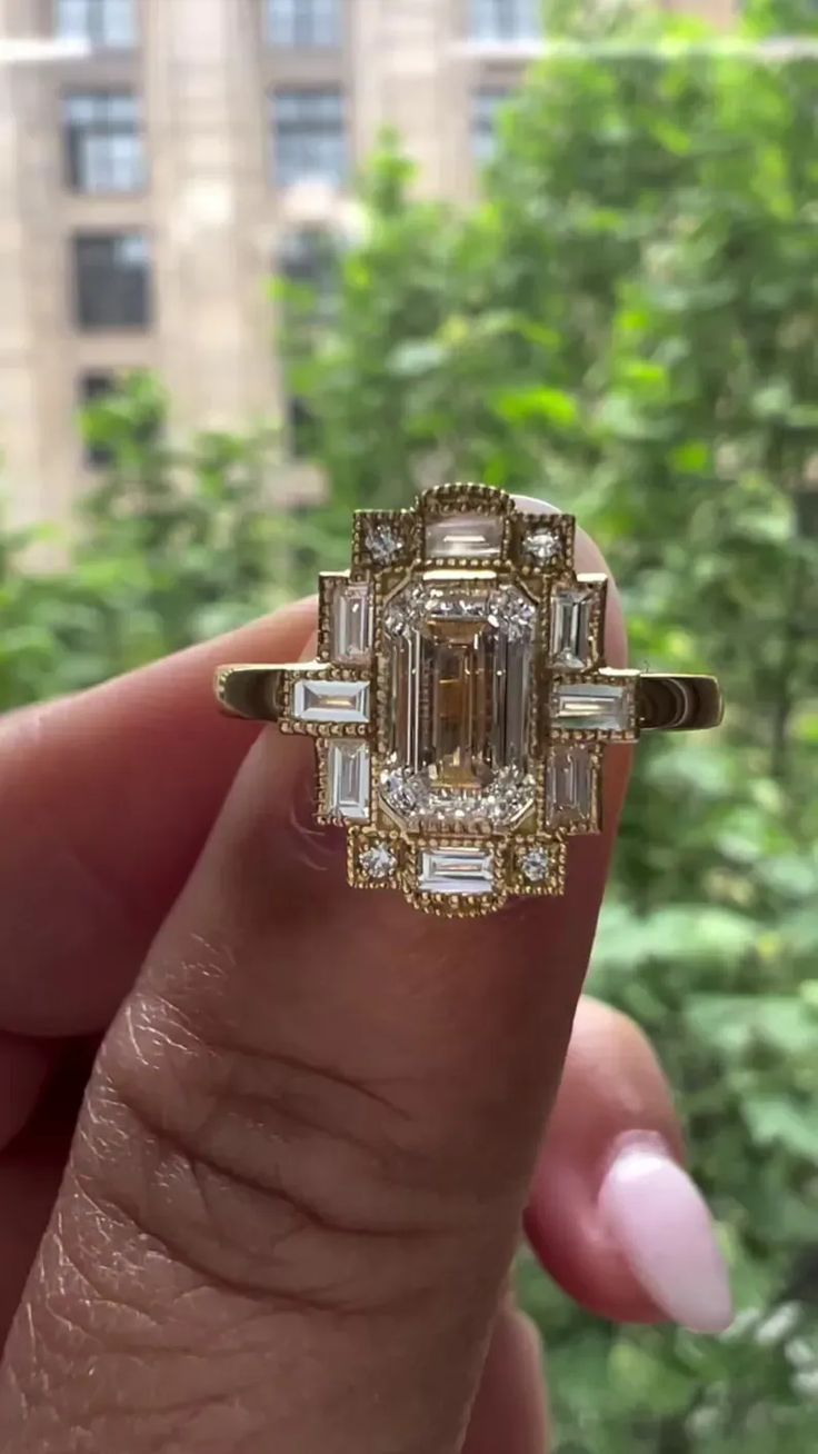 a woman's hand holding an emerald and diamond ring in front of a window