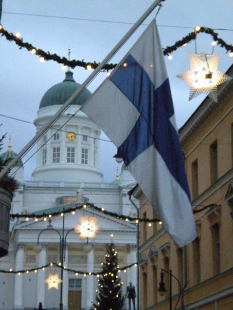 a flag hanging from the side of a building next to a christmas tree with lights on it