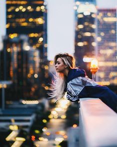 a woman leaning on a ledge in front of city lights