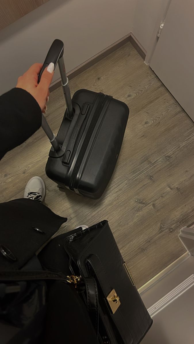 a person holding a piece of luggage on top of a hard wood floor next to a black purse