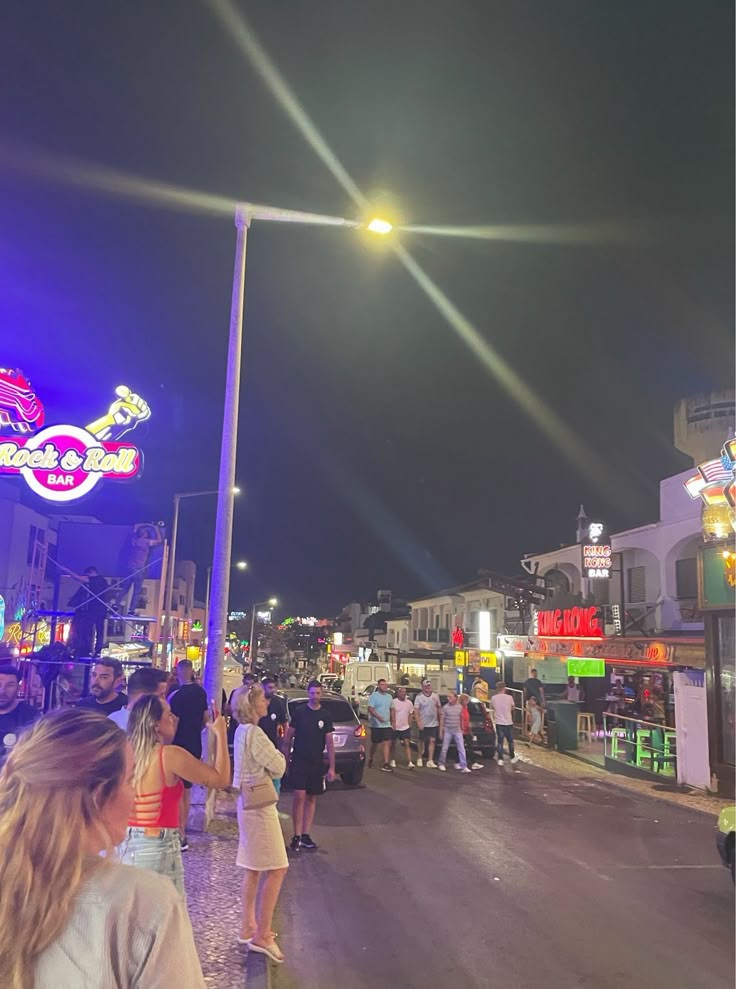 people are standing on the street at night in front of neon signs and buildings with bright lights