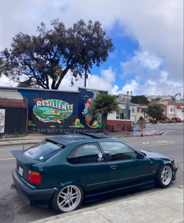 a green car parked in front of a building with graffiti on it's side