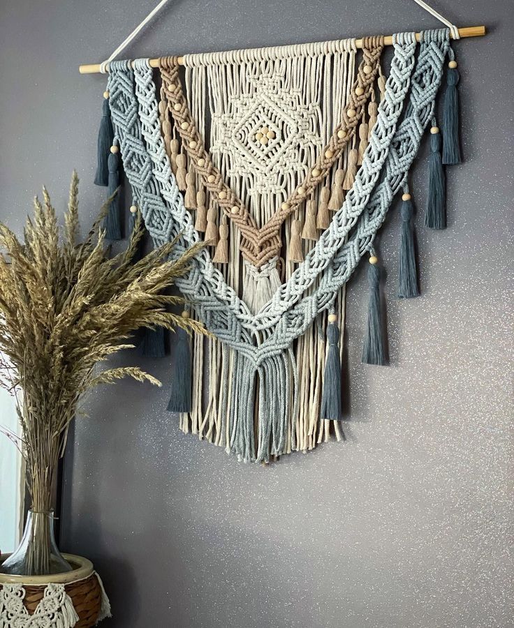 a wall hanging with some tassels and a potted plant next to it