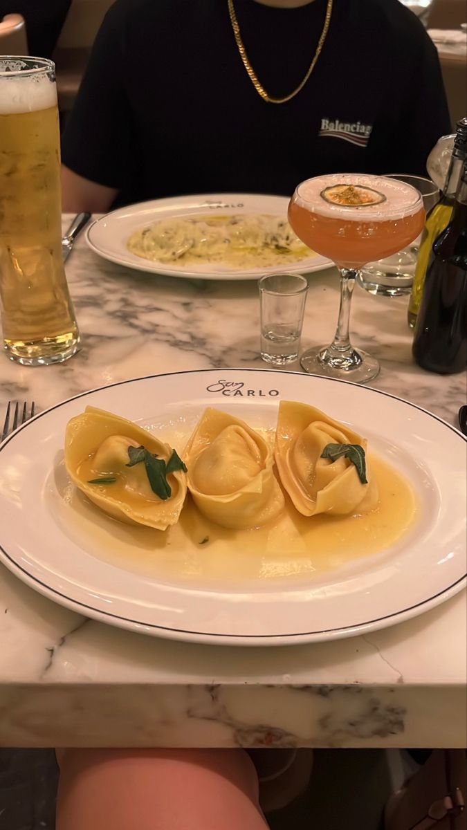 two plates with ravioli on them and a glass of beer in the background at a restaurant