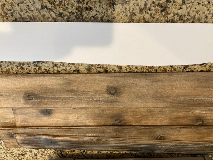 a piece of wood sitting on top of a counter next to a white sheet of paper