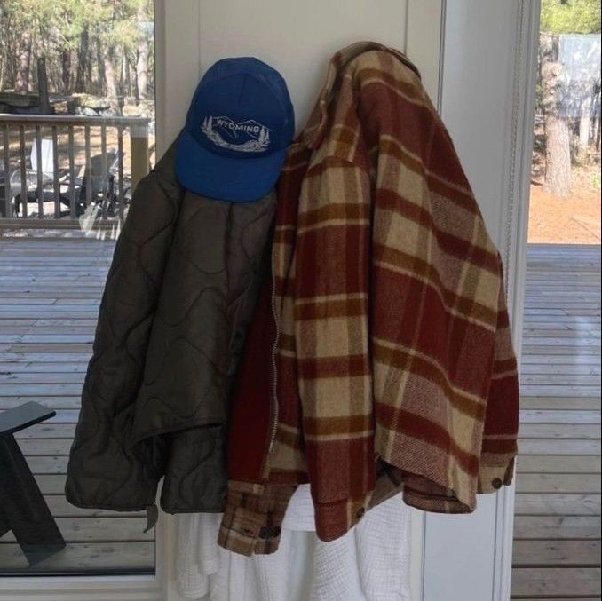 two hats are hanging on a coat rack near a door with a plaid jacket and blue hat