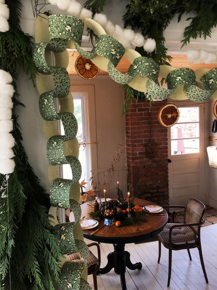 a table and chairs in a room decorated with christmas garlands on the ceiling, lights hanging from the ceiling