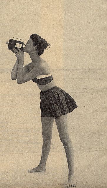 an old photo of a woman on the beach drinking from a water bottle while holding a camera